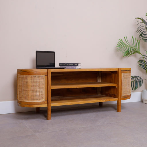 Upgrade your home entertainment center with the spectacular Oriana TV Console. Embodying the core Urban Oak design ethos—where clean, contemporary architectural lines beautifully merge with raw natural luxury—this solid teak media unit is a true triumph of modern organic design.
By combining a warm, hand-polished wood frame with the curved, breathable texture of genuine woven rattan, it establishes immediate warmth and curated designer luxury in your living space. In a furniture market saturated with mass-produced, lightweight particle board and synthetic plastic veneer composites, the Oriana stands tall as a premium legacy piece, hand-shaped to perfection.
Why You'll Love It


Premium Solid Teak Craftsmanship: Meticulously handcrafted from 100% genuine solid teak wood, celebrated for its lifelong durability, high structural density, and rich natural protective oils that provide an exceptionally stable foundation built to securely support large flat-screen TVs.

Iconic Capsule Shape with Hidden Storage: Features an elegant pill-shaped silhouette with smoothly rounded edges. Unlike fully open benches, the Oriana integrates two curved side cabinets with custom doors, blending sculptural Mid-Century architecture with practical, dust-free hidden storage.

Authentic Natural Rattan Accents: The side cabinet doors are inlaid with premium, hand-woven natural rattan cane webbing. This breathable, organic material provides elegant ventilation for enclosed accessories while injecting a soft, sun-drenched Bohemian texture.

Central Open-Access Media Bay: Designed with a spacious two-tier central open shelving layout. This expansive space acts as a perfect, heat-dissipating landing pad for cable boxes, gaming systems, soundbars, and decorative streaming media players.

Product Specifications



Attribute
Details




Material
100% Solid Teak Wood &amp; Authentic Natural Rattan Cane


Shape
Capsule Footprint / Freestanding Pill-Shaped Entertainment Unit


Style
Mid-Century Modern / Organic Boho / Japandi Minimalist / Coastal Chic


Finish
Hand-Polished Natural Satin Teak Tone


Storage Configuration
2 Central Open Shelves &amp; 2 Enclosed Curved Side Cabinets


Overall Dimensions
151.8 cm (Length) × 55 cm (Height) × 46 cm (Depth)


Usage
Ideal for Living Rooms, Media Lounges, and Premium Sitting Rooms


